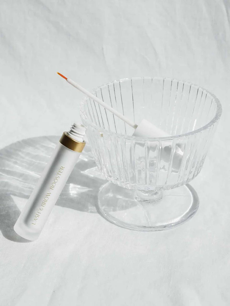 Das Glas Stärkendes Wimpernserum liegt angelehnt auf einer Schüssel in der die bürste von dem Produkt