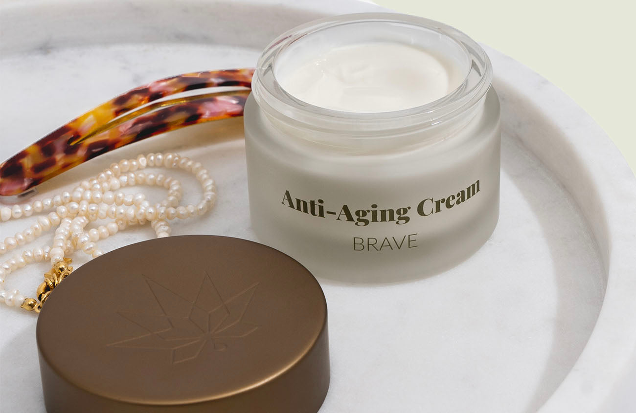 Anti-Aging-Creme mit Haarspange und Perlenkette auf weißer Platte
