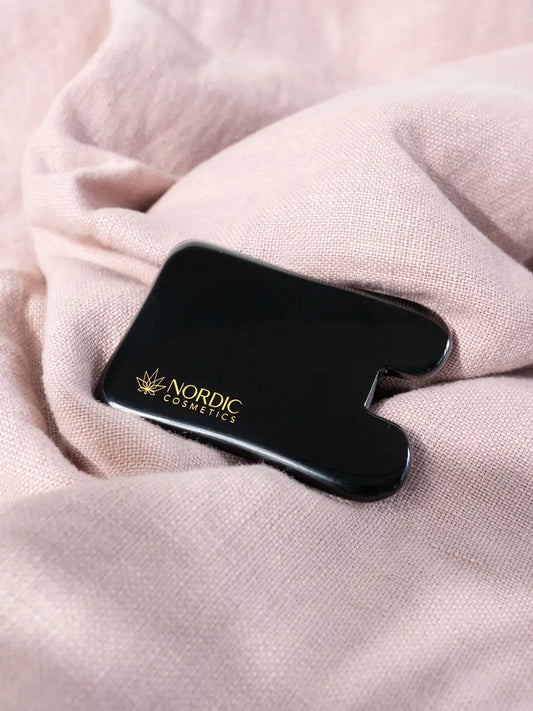 Gua Sha von Nordic Cosmetics auf einem rosa Tuch.