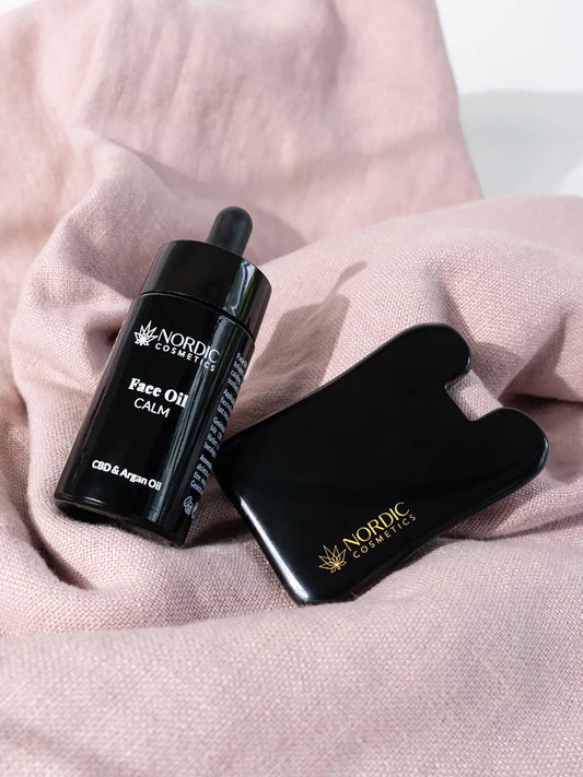 Gua Sha und Gesichtsöl von Nordic Cosmetics auf einem rosa Tuch.