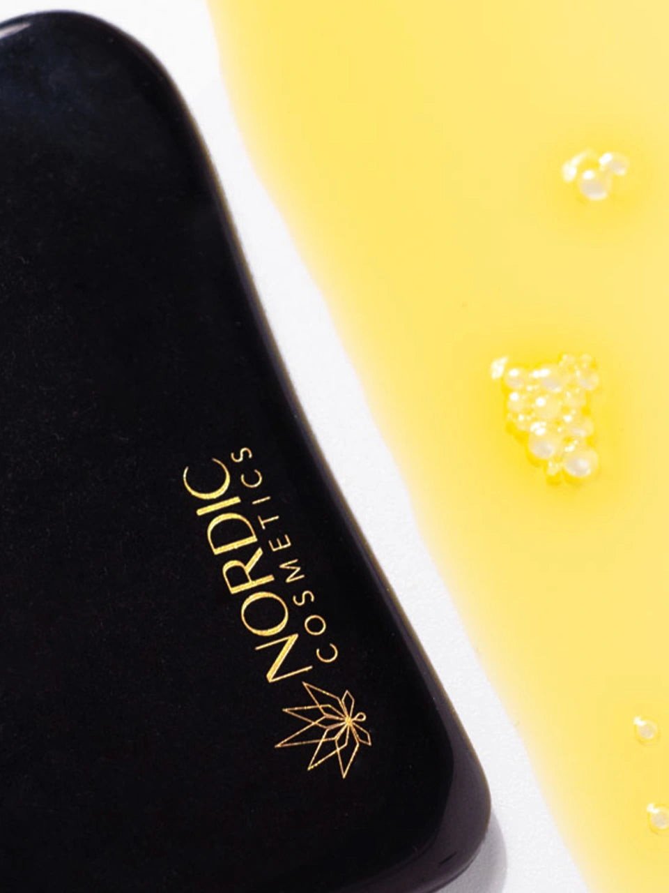 Obsidian Gua Sha von Nordic Cosmetics ist neben einer gelben Flüssigkeit abgebildet.