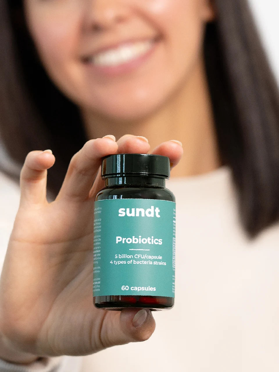 Das Probiotikum von Sundt wird von einer lächelnden Frau in die Kamera gehalten.