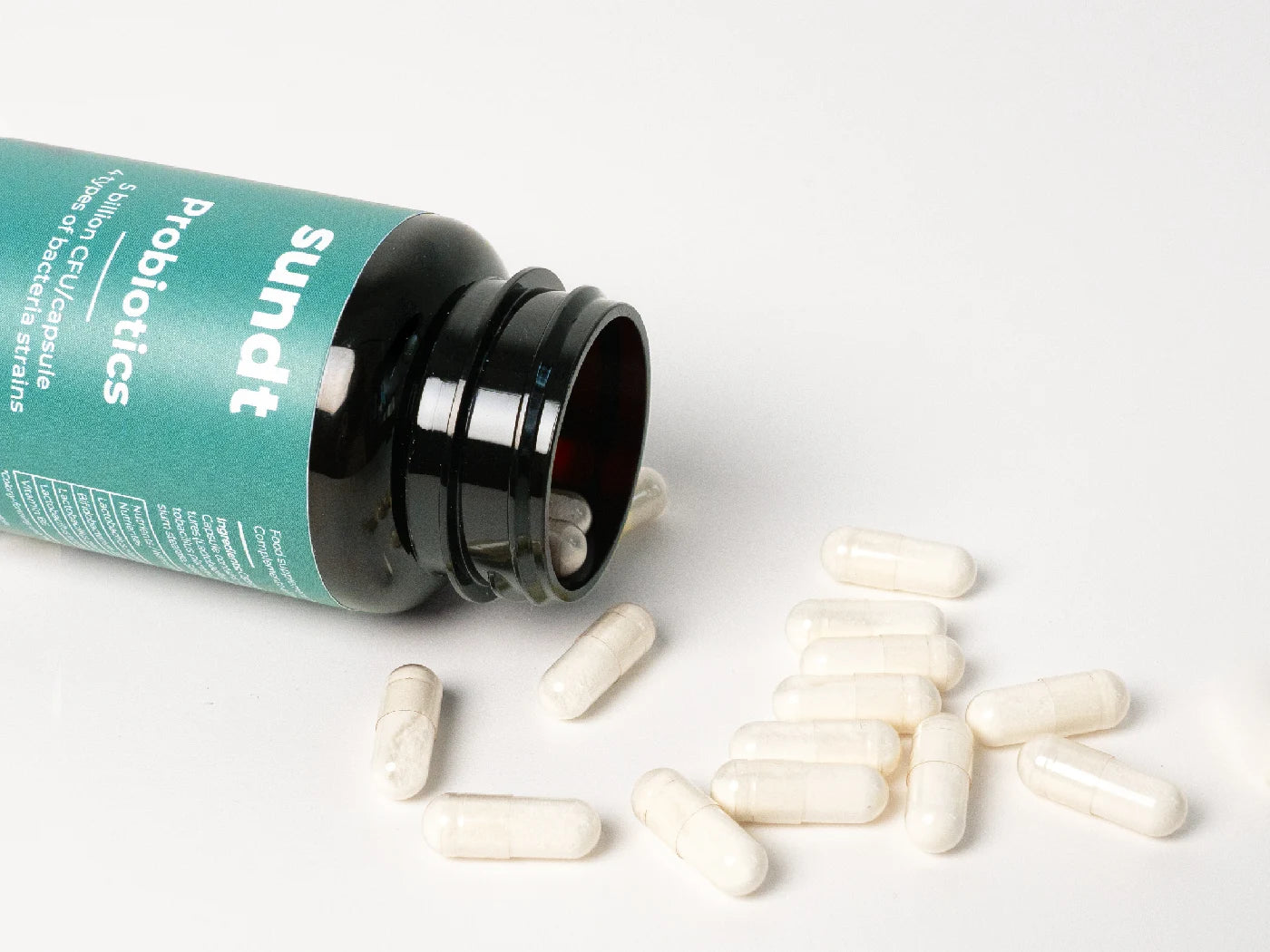 Das Probiotikum von Sundt liegt offen auf einem weißen Hintergrund, und die Kapseln fallen heraus.