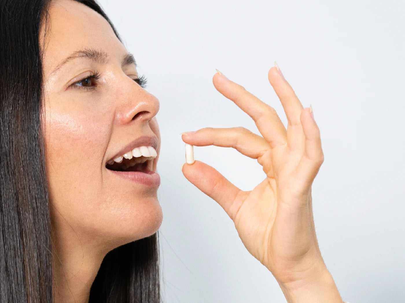 Eine Frau mit braunen Haaren hält eine weiße Kapsel in der Hand. Sie führt sie zum Mund.