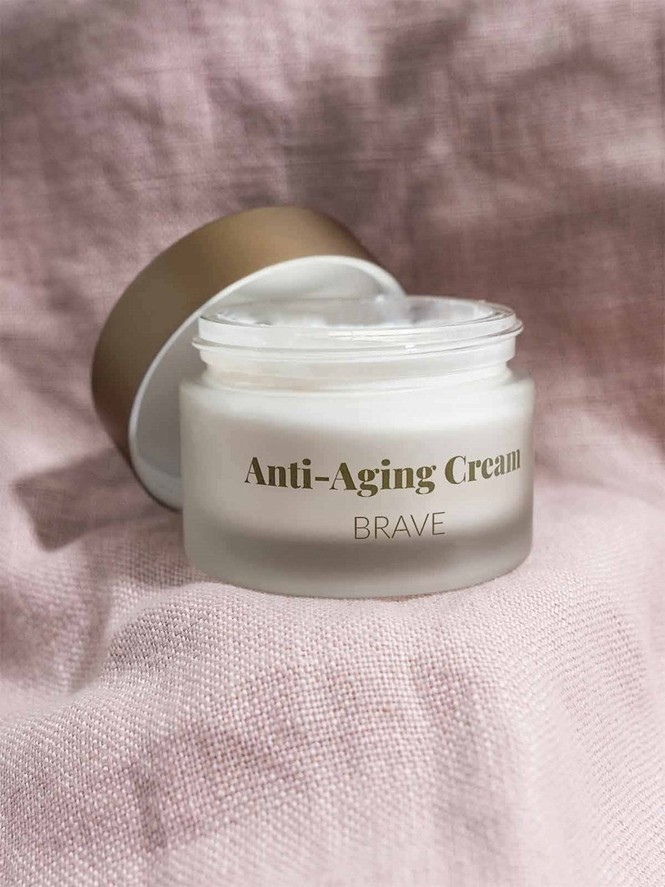Eine offene Dose des Revitalisierende Anti-Aging Creme mit CBD liegt auf einem pinken Tuch.