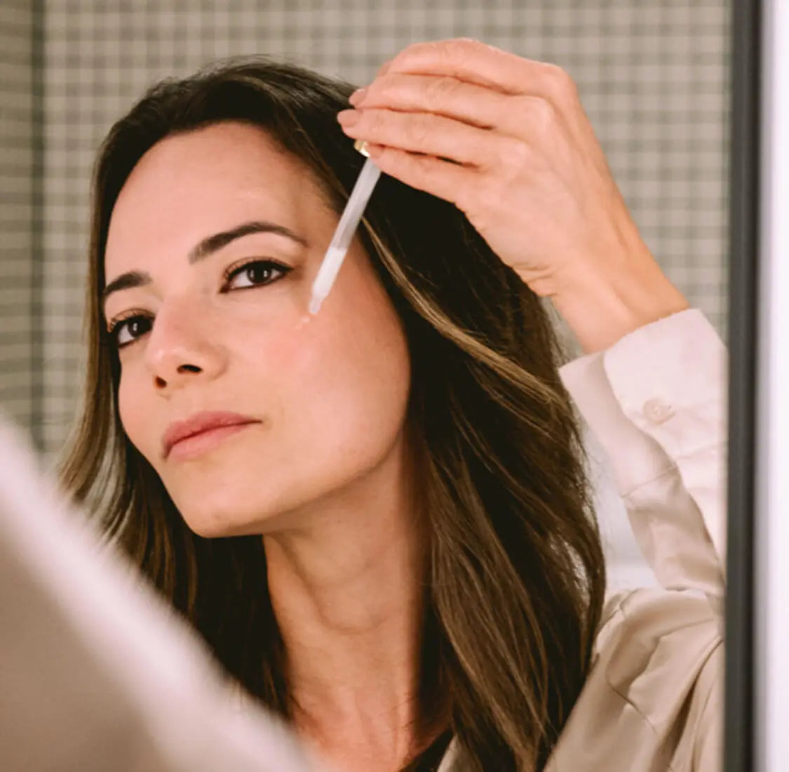 Frau trägt vor dem Spiegel Feuchtigkeitsspendendes Gesichtsserum auf ihr Gesicht auf