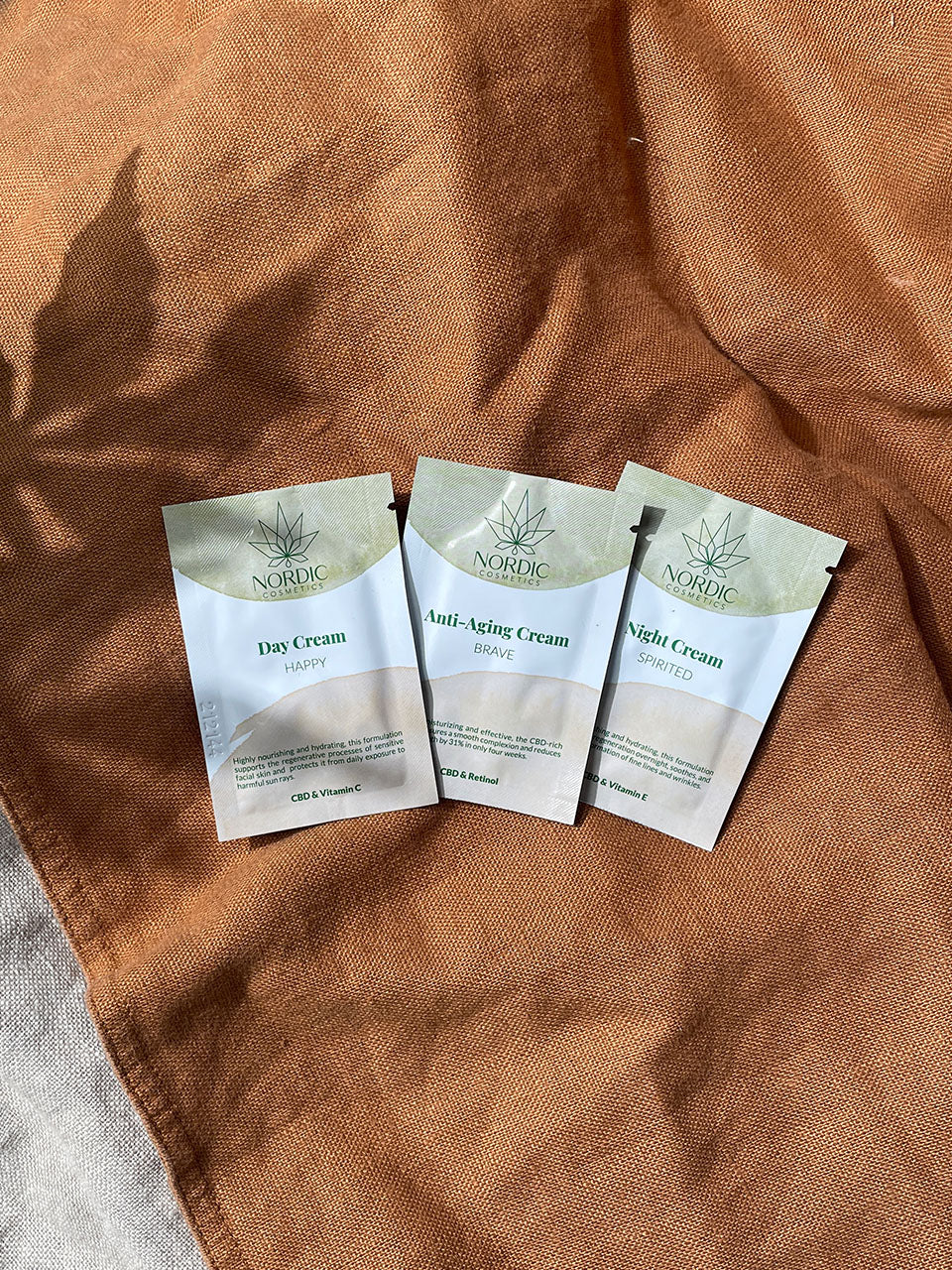 Tagescreme, Nachtcreme und Anti-Aging-Creme von Nordic Oil sind auf einem braunen Tuch ausgelegt.