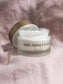 Eine offene Dose des Revitalisierende Anti-Aging Creme mit CBD liegt auf einem pinken Tuch.